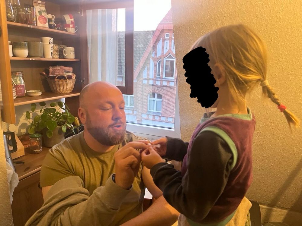 Ich sitze auf einem Stuhl, die Fünfjährige steht neben mir auf einem Stuhl. Wir halten gemeinsam eine Spritze einer Grippeimpfung in der Hand und schauen sie an.