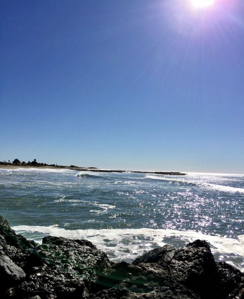 The sun is shining on the oceans and black rocks along the shores.