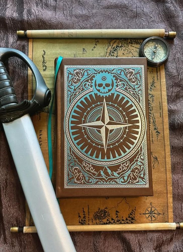 Special edition of "Echoes of the Imperium" with brown faux-leather hardcover, teal and silver foil, and teal ribbon bookmark, laid out atop a map with a compass and sabre laid out nearby.