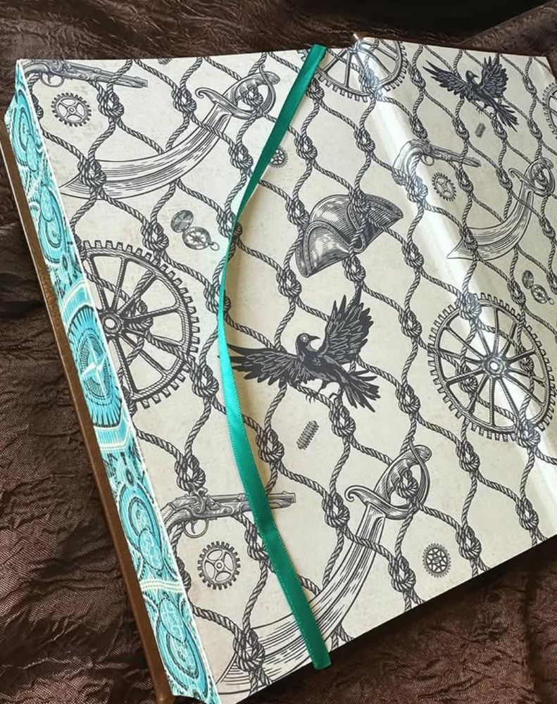 Special edition of "Echoes of the Imperium" with brown faux-leather hardcover, teal and silver foil, and teal ribbon bookmark. The book is open, revealing the rigging, flintlock, tricorne and blackbird endpapers peppered with ornamental cogs.