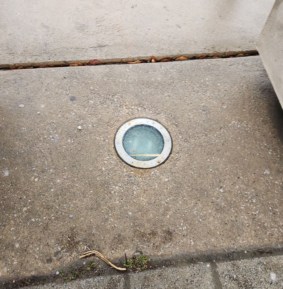 An outdoor light embedded in the pavement that looks similar to the one used in the artwork of the Death Grips album "The Powers That B".