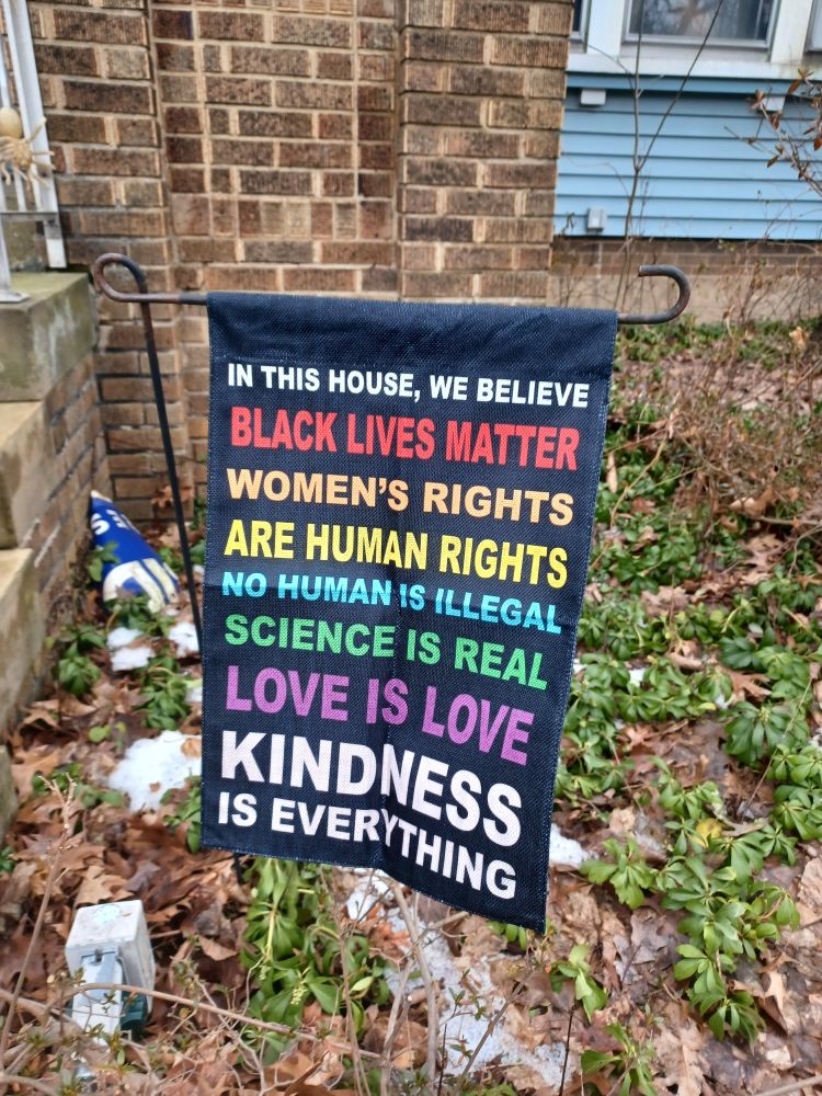 Flag says: In this house, we believe Black Lives Matter Women's rights are human rights,no human is illegal, science is real, love is love, kindness is everything 