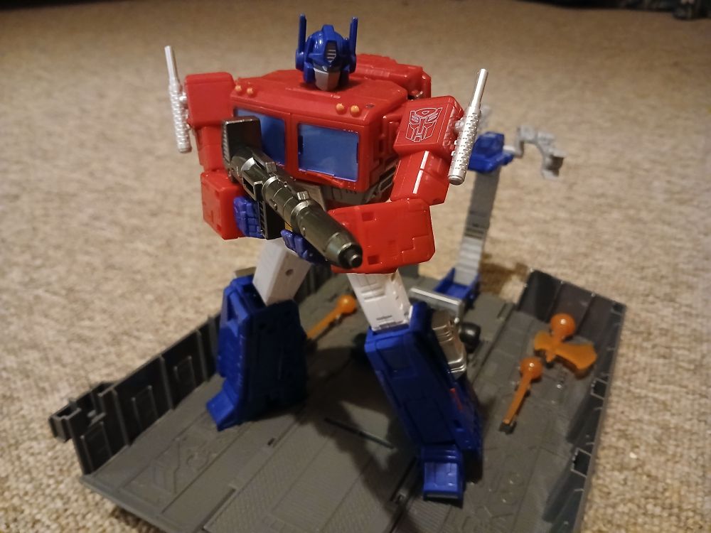 Studio Series 86 Optimus in robot mode stood on his open trailer holding his gun across his chest 