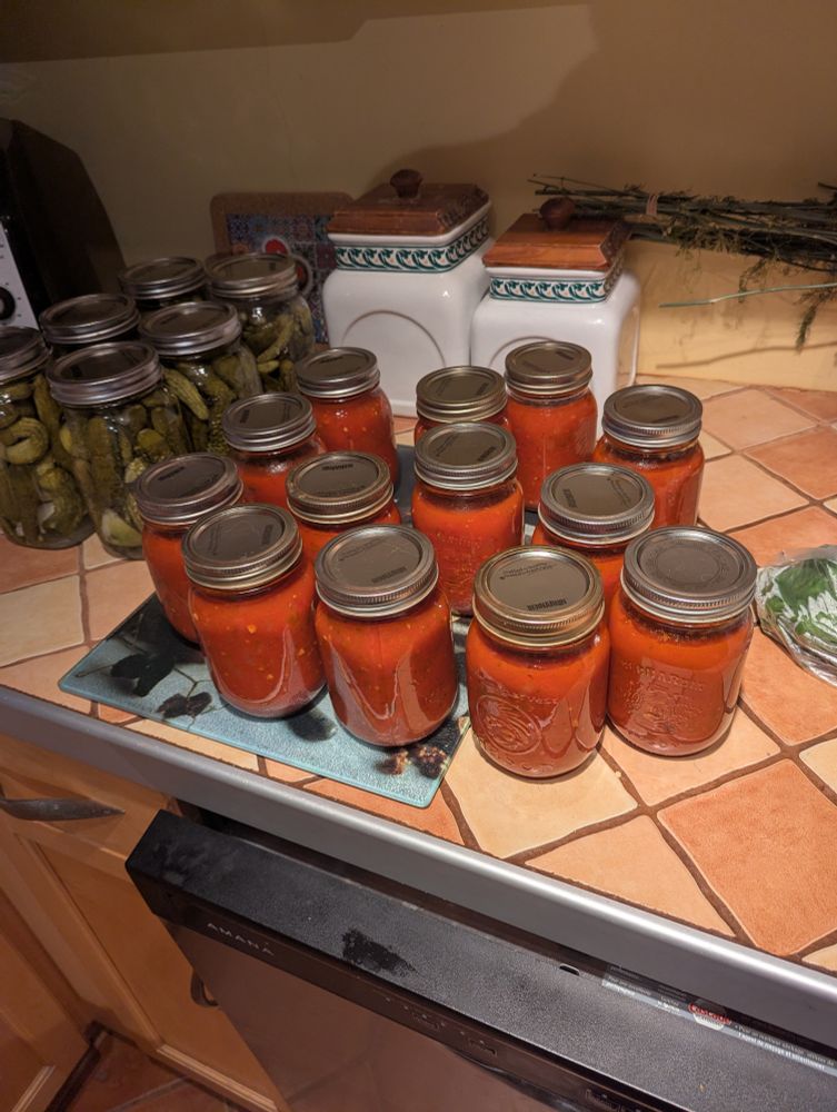 Bottled tomato sauce on a tile counter. Bottles of dill pickles in the background 