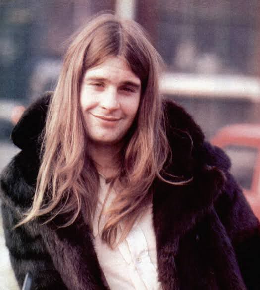 Ozzy Osbourne jovem. Ele olha pra câmera com cabelos longos e uma jaqueta de pelinhos