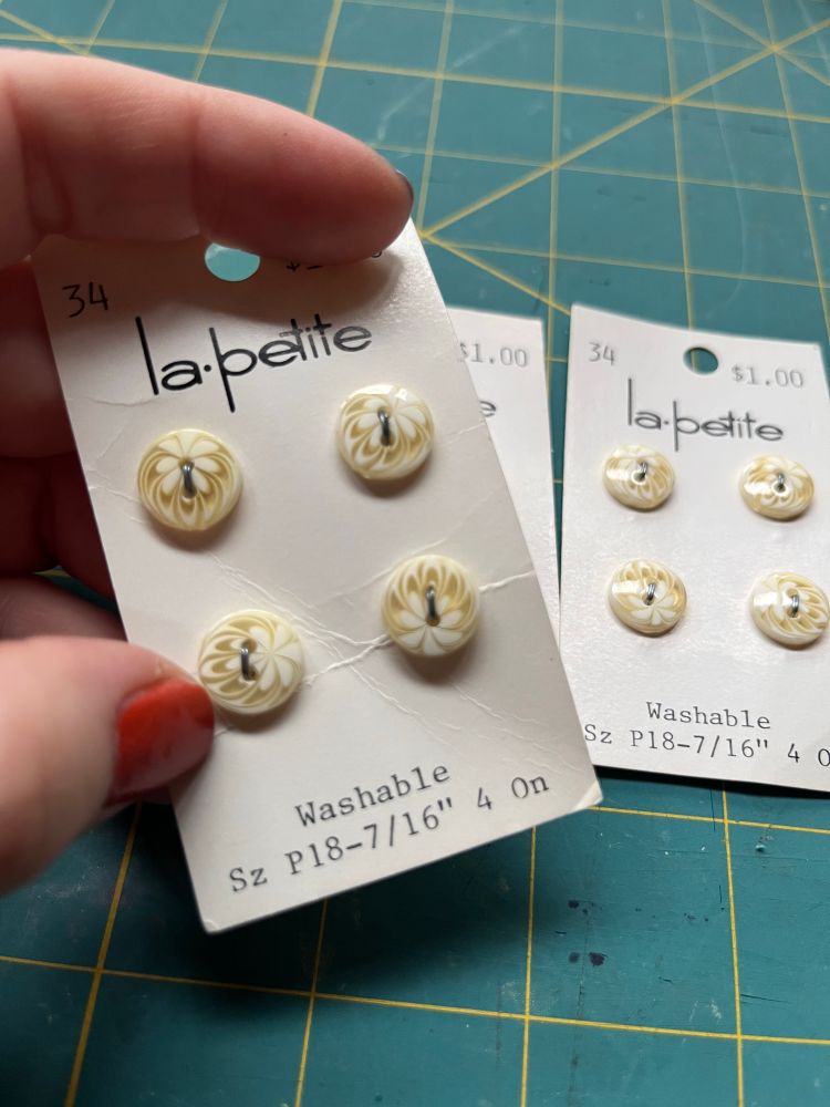 Several cards of buttons each with 4 white and cream 7/16” buttons on them. The buttons have a kind of swirly design that looks almost like latte art or a flower? 