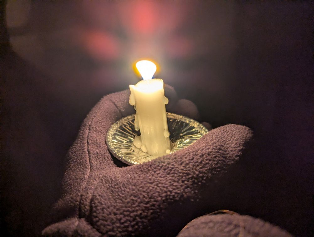 A candle held in gloved hands. 