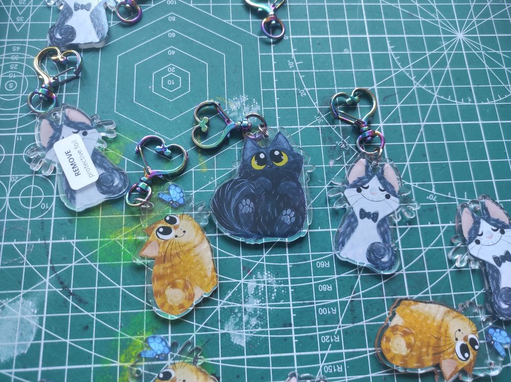 Various cat Keychains (orange, void, tuxedo) in a green cutting mat