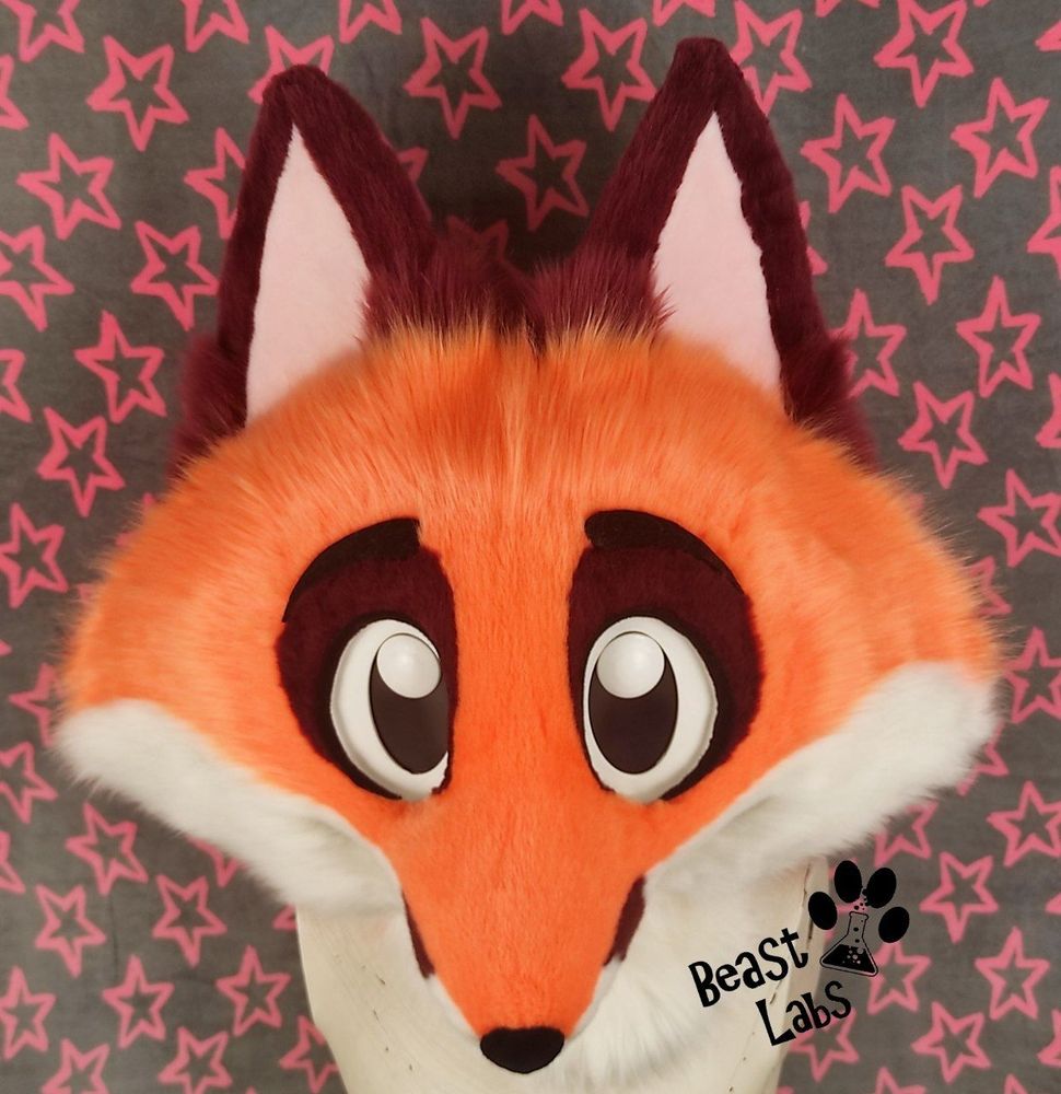 Photo of a bright orange, white and bordeaux coloured fox costume head with big cartoony eyes.