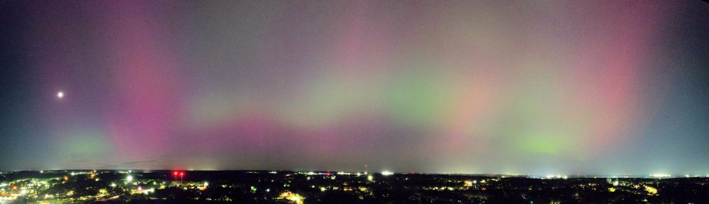 Panorama of night sky over the city with red and green aurora. Slightly more than 180 degree view.