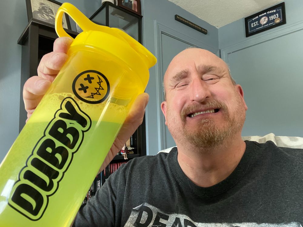 a man smiling holding up a yellow shaker with the word Dubby on it and a smiling face logo