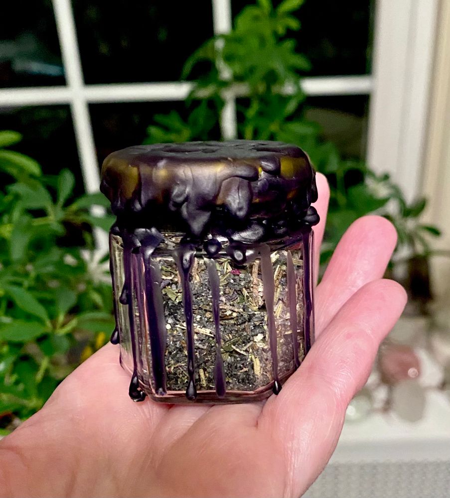 Glass spell jar filled with dried herbs and crystals, sealed with black wax. 