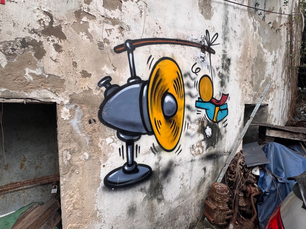 A photo of some street art. There is a desk fan with yellow blades. It is on.

From the top is a stick with a piece of string tied to it. Then tied to that is a little person pretending to fly in front of the fan