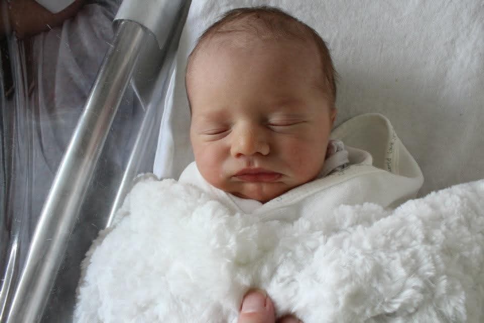 A perfect sleeping newborn, swaddled in his hospital bassinet with a fluffy white blanket. 