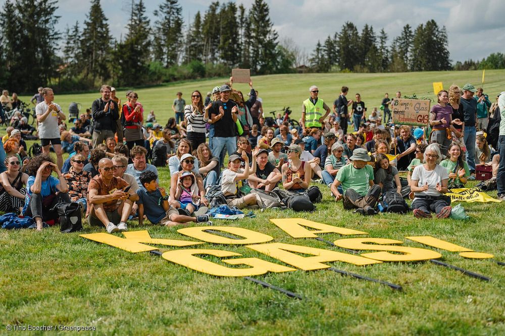 Viele menschen sitzen auf einer Wiese, davor der Schriftzug "Koa Gas".