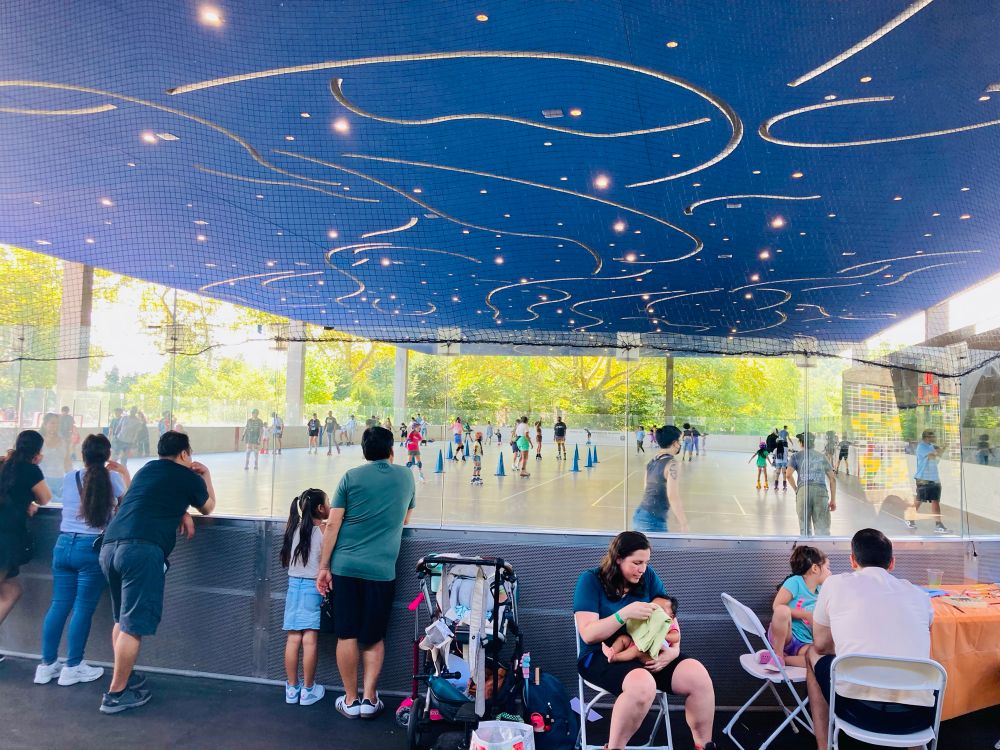Covered rink on which there are roller skaters, with spectators standing along the perimeter, at LeFrak Center at Lakeside at Prospect Park in Brooklyn. August 3, 2025.