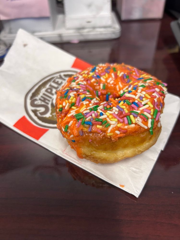 Donut with sprinkles and orange icing sitting on a Shipley Donuts bag 