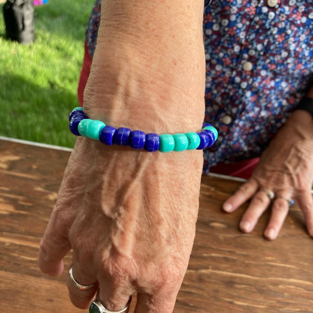 A bracelet being modeled by a grandmothers hand, with light and dark blue beads in a growing pattern-one of each then two and three etc