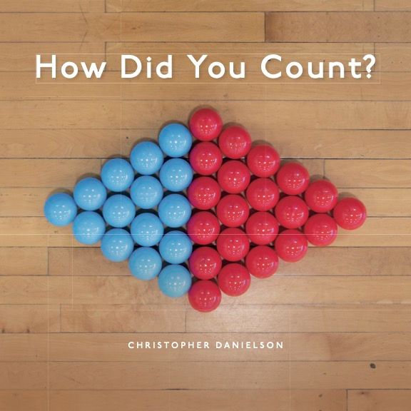 Book cover for How Did You Count? There is a sideways diamond of shiny plastic spheres carefully arranged on a wood floor. The left "half" of the diamond is a triangle with base five, made of light blue spheres. The larger, right "half" is a triangle with base six, made of red spheres.