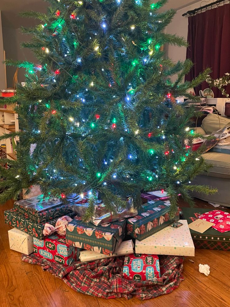 Christmas tree with green, red, and white lights with multiple wrapped presents in green, white, and red paper under it 