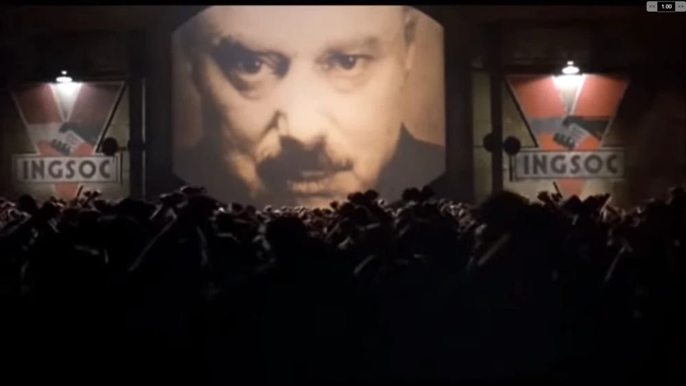 Image taken from movie '1984'. In it we see a crowd in front of a screen with the face of Big Brother.