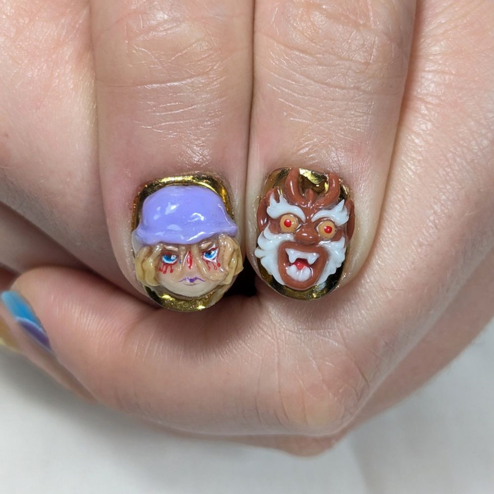 Two thumbs put next to each other featuring a handsculpted charm on each of them. One with Kusuriuri the protagonist of Mononoke and the other with the youkai-like head on the pommel of his sword.