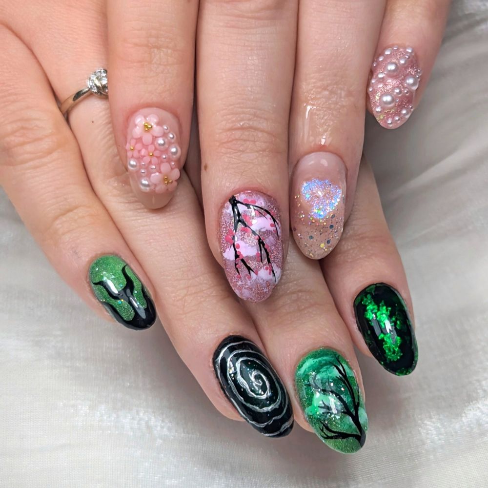 Two hands placed one on top of another featuring a Wicked-themed gel manicure. The hand on the bottom has predominantly black and green nails for Elphaba and the hand on the top is pink for Glinda.