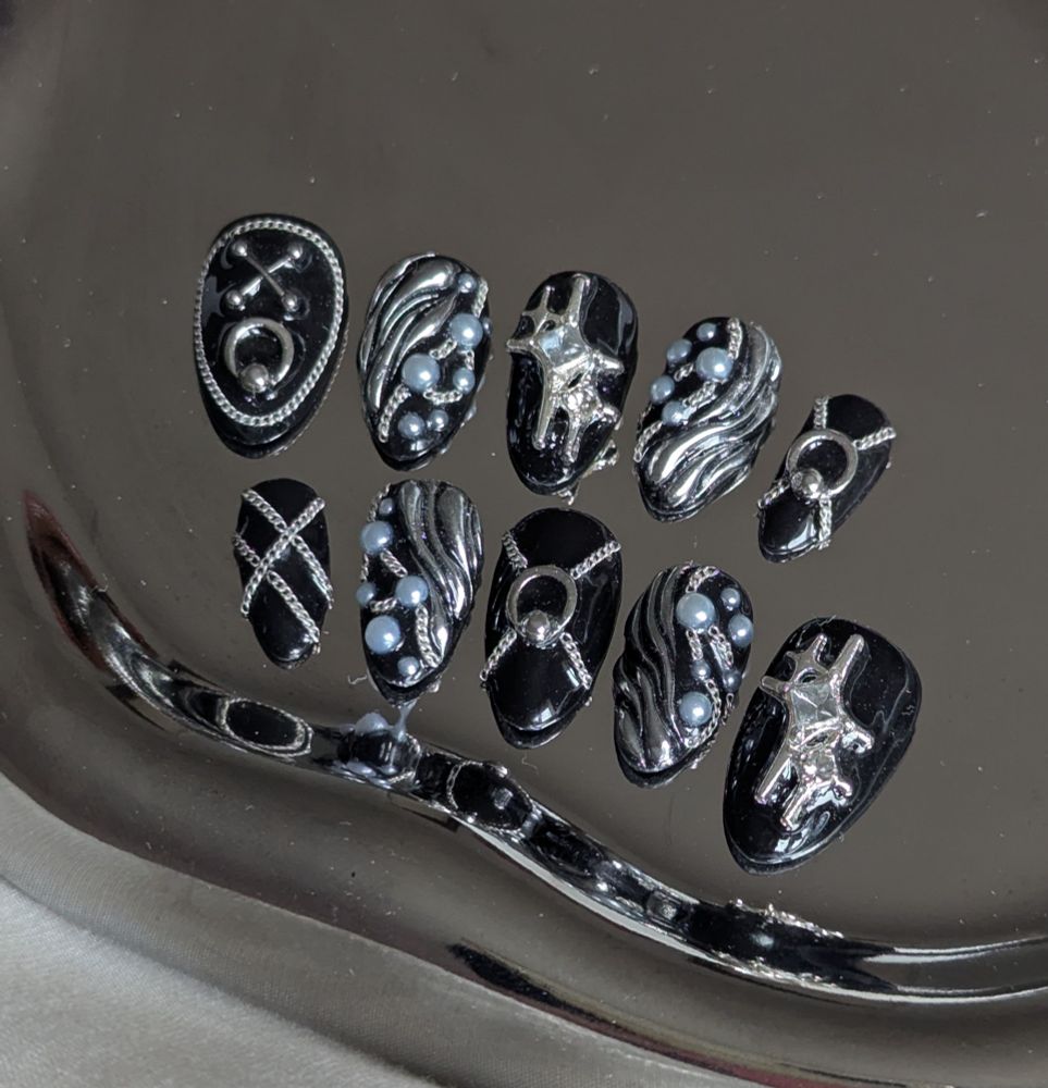 A set of 10 black press on nails in short almond shape. They featured numerous silver chains, charms and pearls arrangements and also silver chrome 3D on some nails.