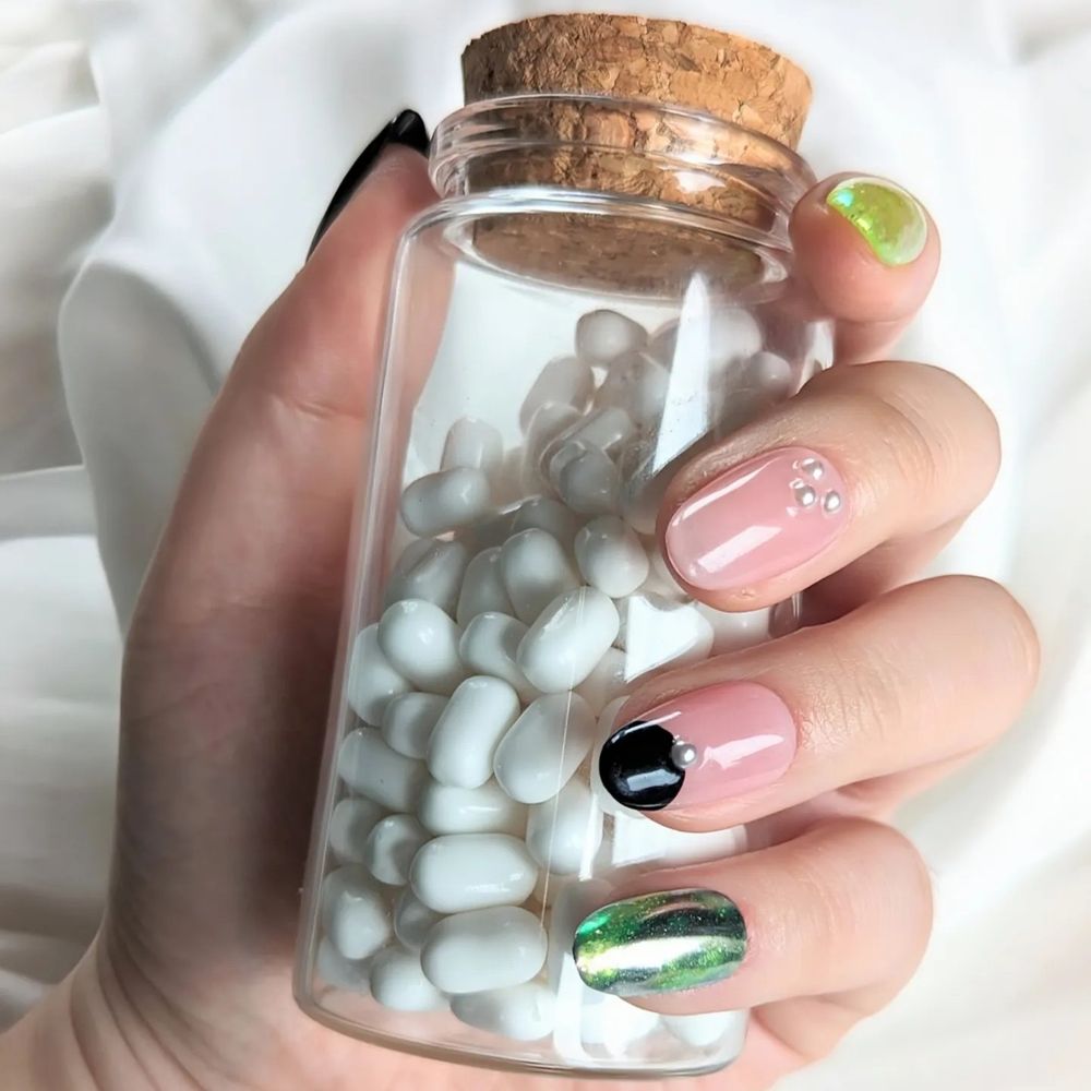 Une main qui tient un flacon en verre rempli de dragées blanches et qui reproduit une case du manga Magic Nail Art. Le but est de mettre en valeur les faux ongles portés.