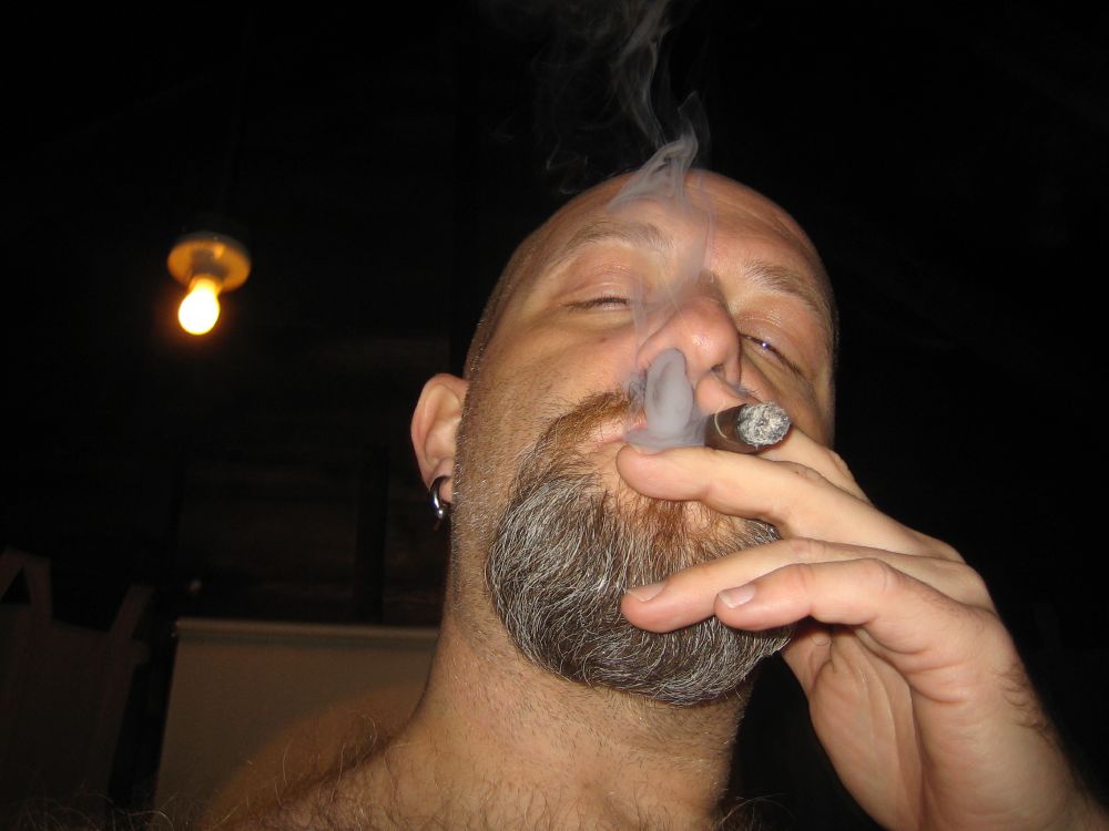 Close up of a man with bald head and goatee smoking a cigar.