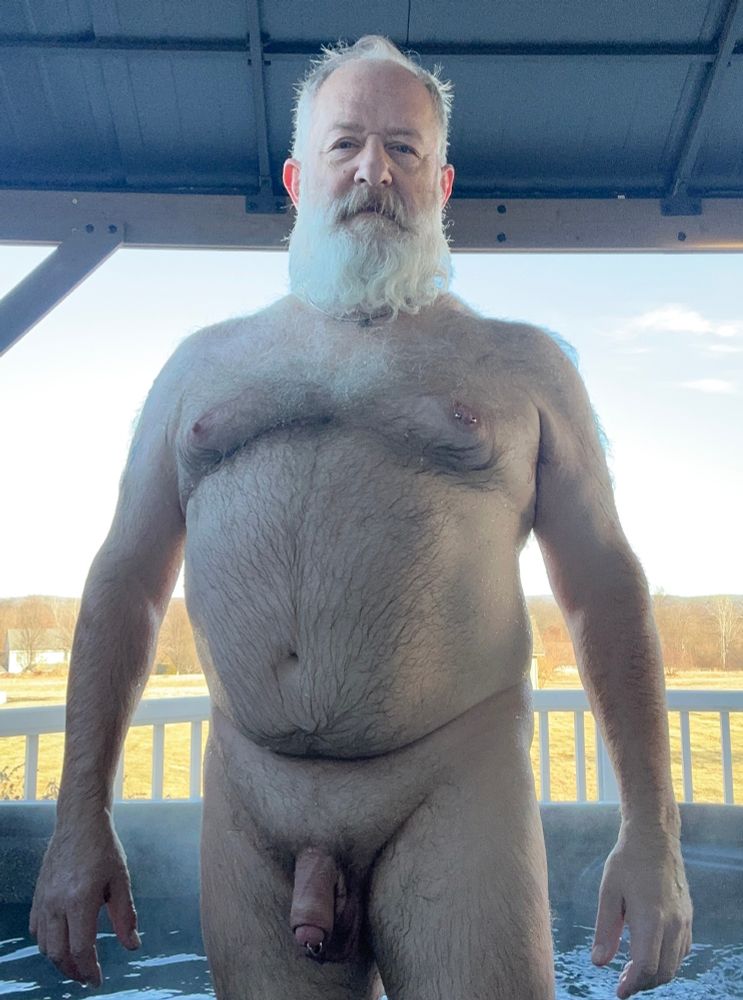 Hairy bearded man standing naked in a hot tub from head to thighs showing hairy chest and soft fat cock.