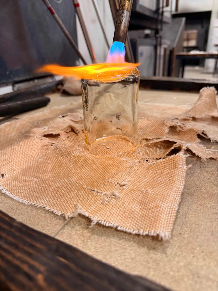 A finished cup on a table, with fire blowing on the bottom to smooth it out