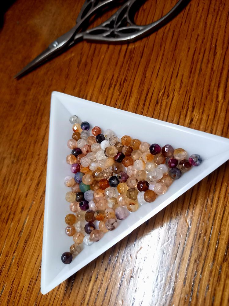 カットの入ったラウンド型の天然石のビーズが、三角の白いトレーに入っている写真です。