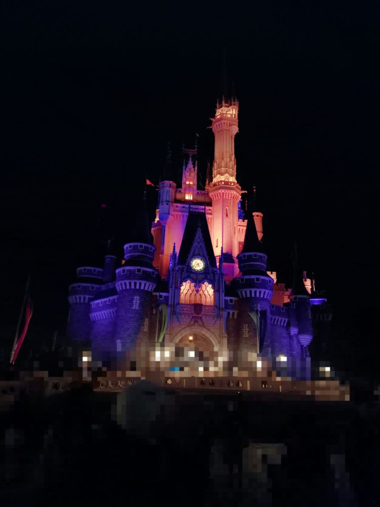 夜のシンデレラ城の写真です。下部が紫、上部がオレンジのハロウィンカラーのライトアップが施されています。