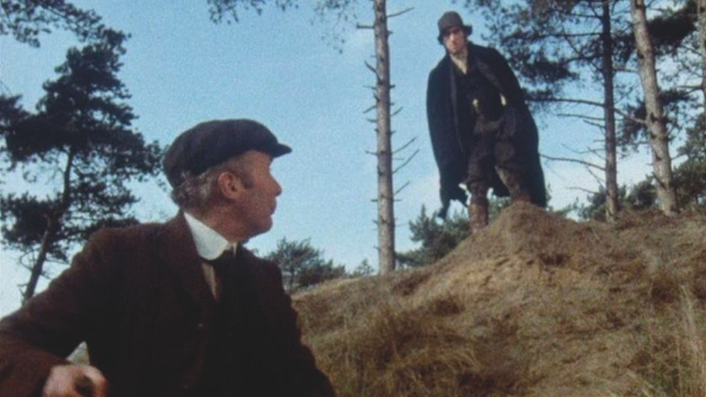 An amateur archeologist looks up from his dog at a figure in black looming over him - "No digging here", the figure warns....