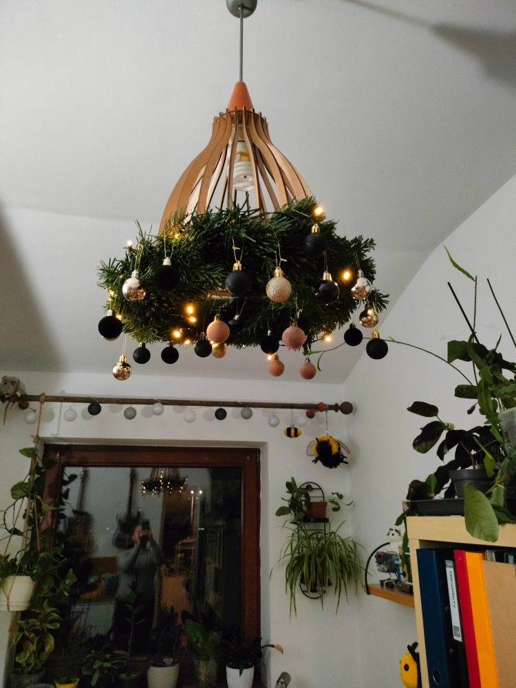 podłaźniczka powieszona na drewnianym żyrandolu - wianek z gałązek jodłowych, obleczony drobnymi światełkami i małymi złotymi i czarnymi bombkami