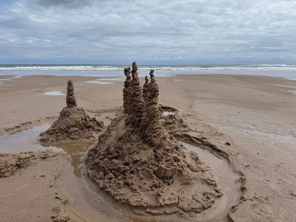 Towering sandcastle with water filled moat and waves in the background 