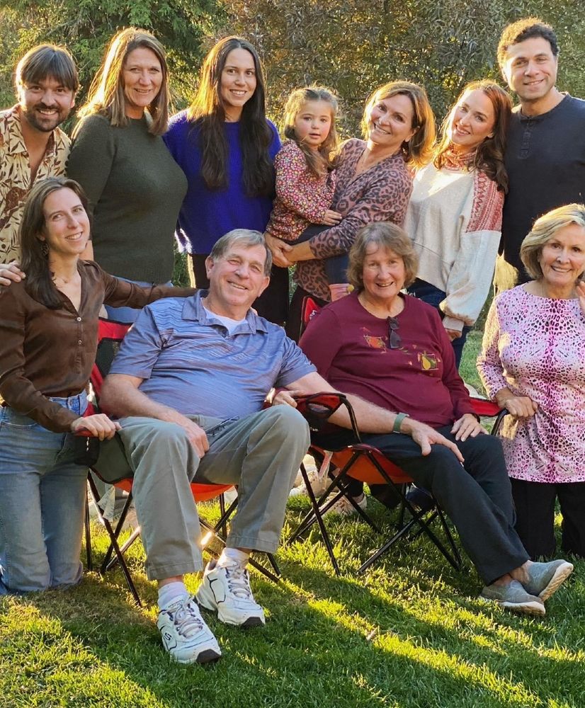 Group family photo taken outside with everyone standing around an older couple who are sitting in chairs.