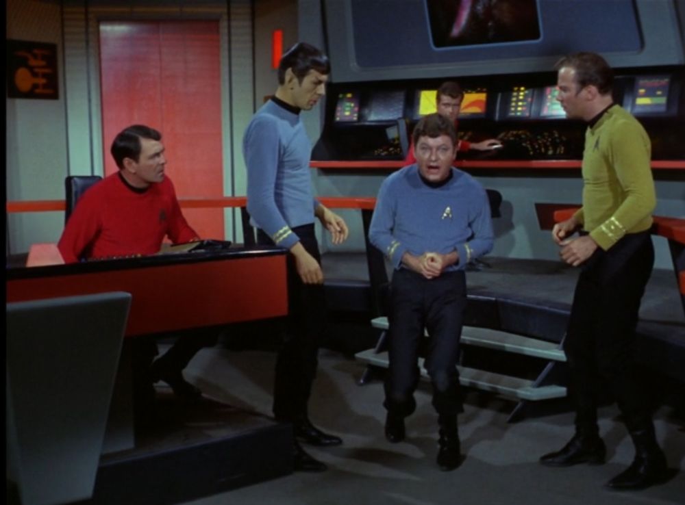 TOS scene on the bridge.  Kirk & Spock are standing next to Dr McCoy as he begins to flip out after accidentally injecting a full ampule of cordrazine into himself.  Mr. Leslie is off the hook.  He's a few steps away at the engineering station in the background.