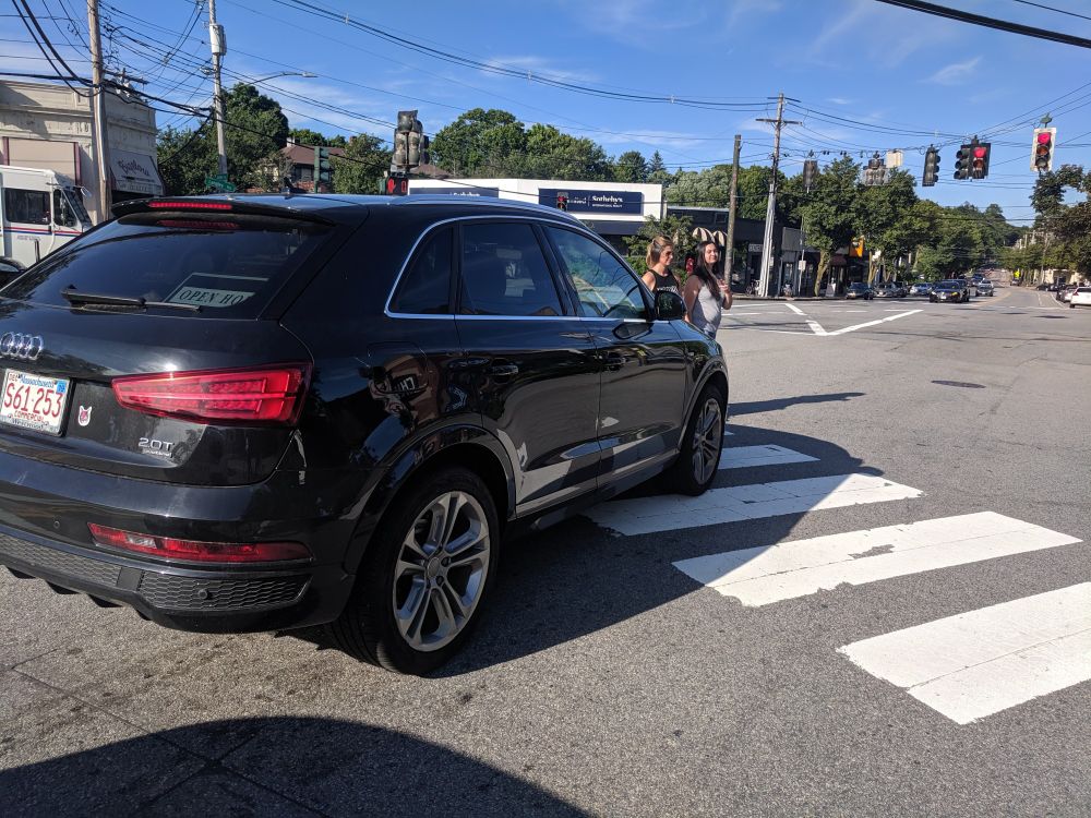 Black Audi SUV blocking the crosswalk at a red light.  Peds are walking in front of it.
