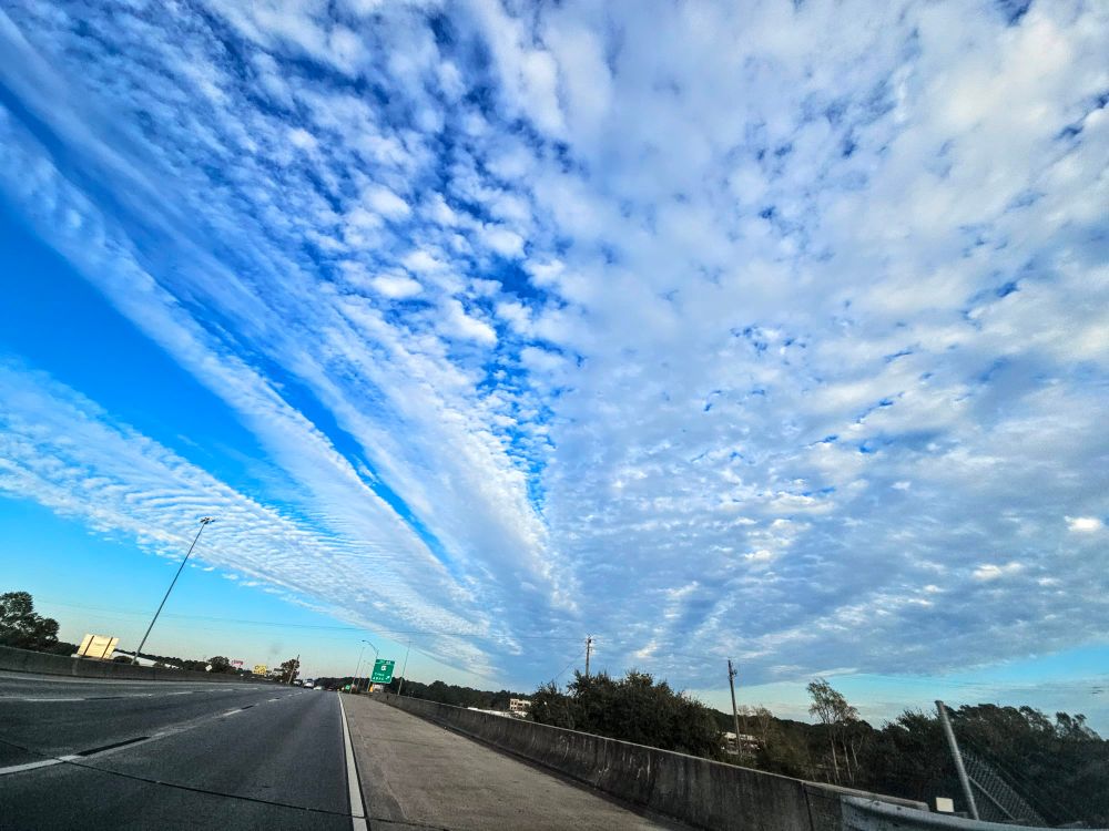 An image of the sky with linear clouds leading to a vanishing point in the distance.  A road is below, leading to a different point on the horizon. 