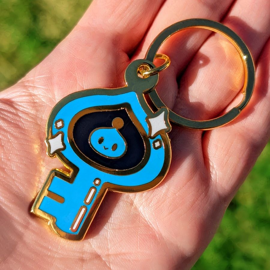 Product photo of my palm holding a keychain inspired by the Chao Key from Sonic Adventure 2. The hard enamel design measures 2", and it hangs from a golden ring-shaped keychain.