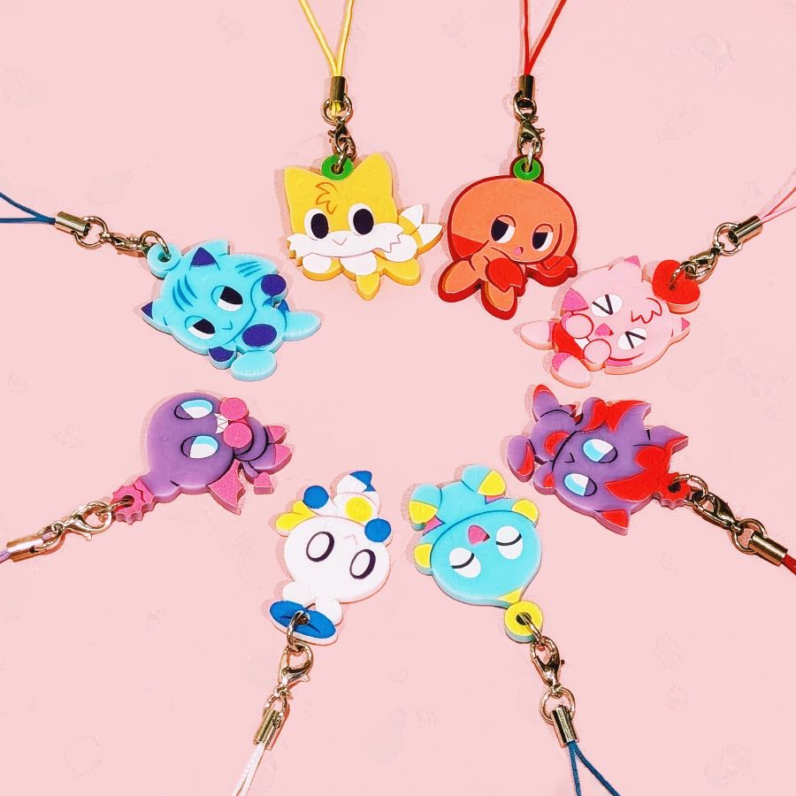 Product photo featuring 8 Chao charm designs from Sonic Adventure 2—Sonic Chao, Tails Chao, Knuckles Chao, Amy Chao, Shadow Chao, Chao, Hero Chao, and Dark Chao—arranged in a neat circle against a pink backdrop. All charms are approximately 1.5" and single-sided on colored acrylic, and they each hang from a colorful lanyard strap.