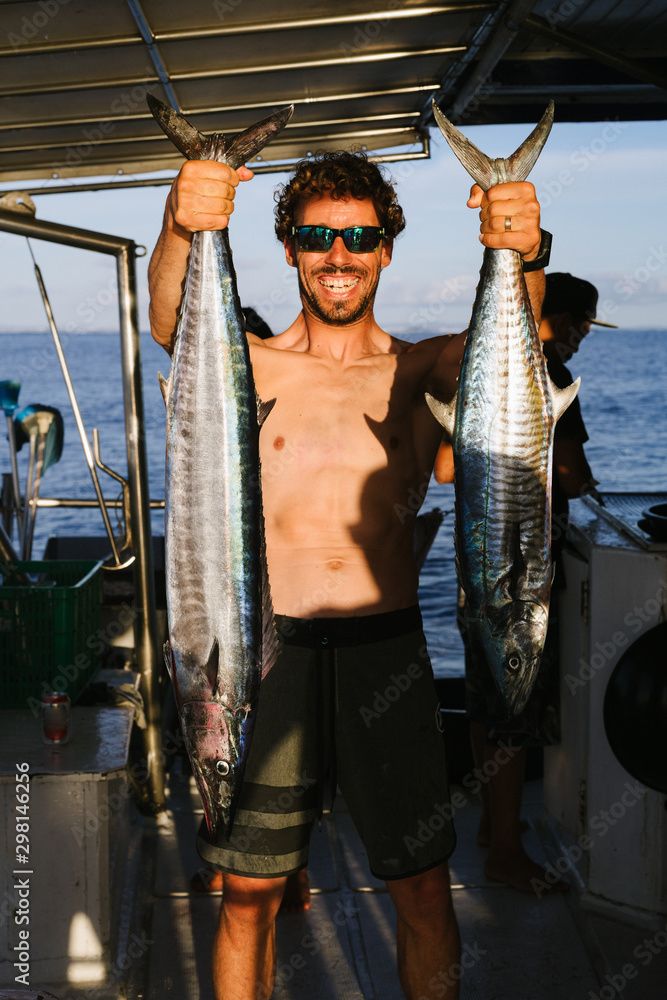 A man is holding two big fish, one in each hand. 
