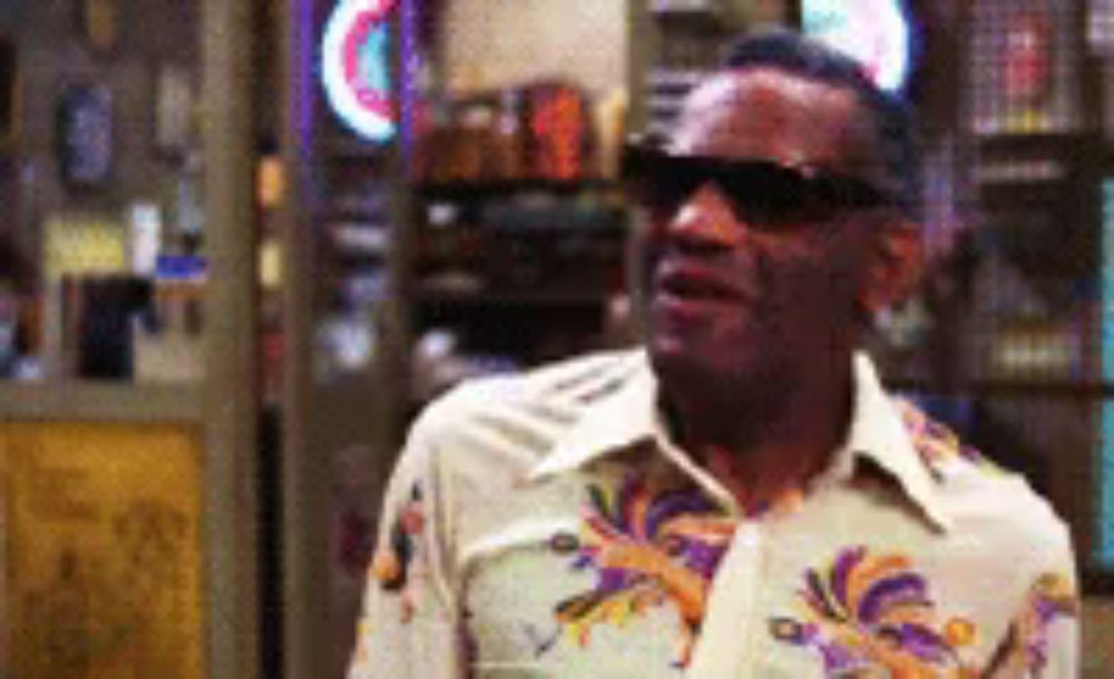 a man wearing sunglasses and a hawaiian shirt is standing in a room .