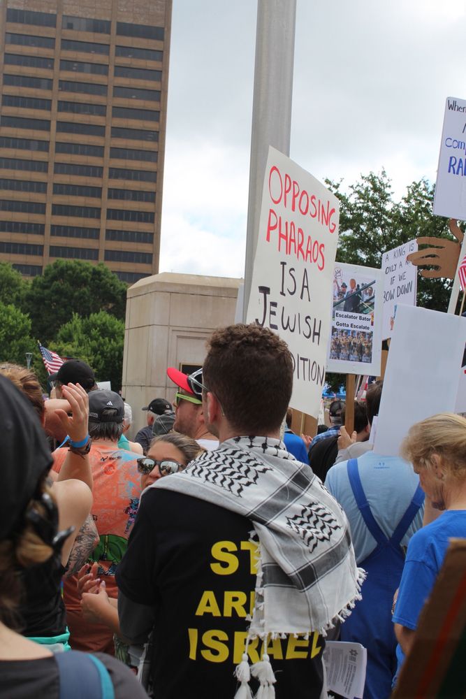 A protester wears a Keffiyeh next to a sign that reads “opposing pharaohs is a Jewish tradition”  