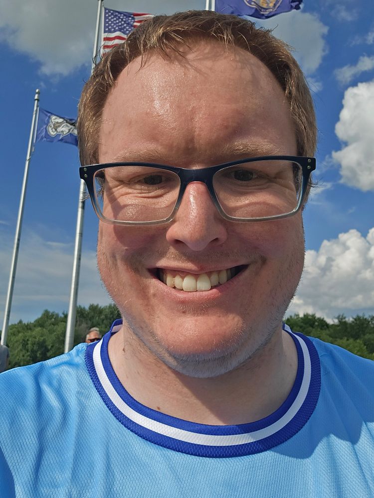 Poster is smiling in photo with a blue jersey on and two flags in the background