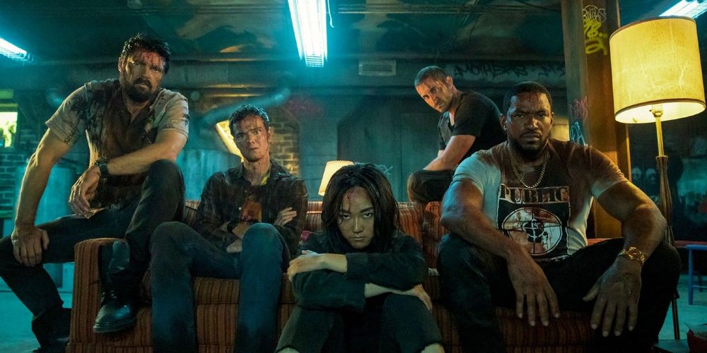 Frame de la segunda temporada de The boys, con todo el grupo ensangrentado, con caras serias, viendo la televisión en su escondite.