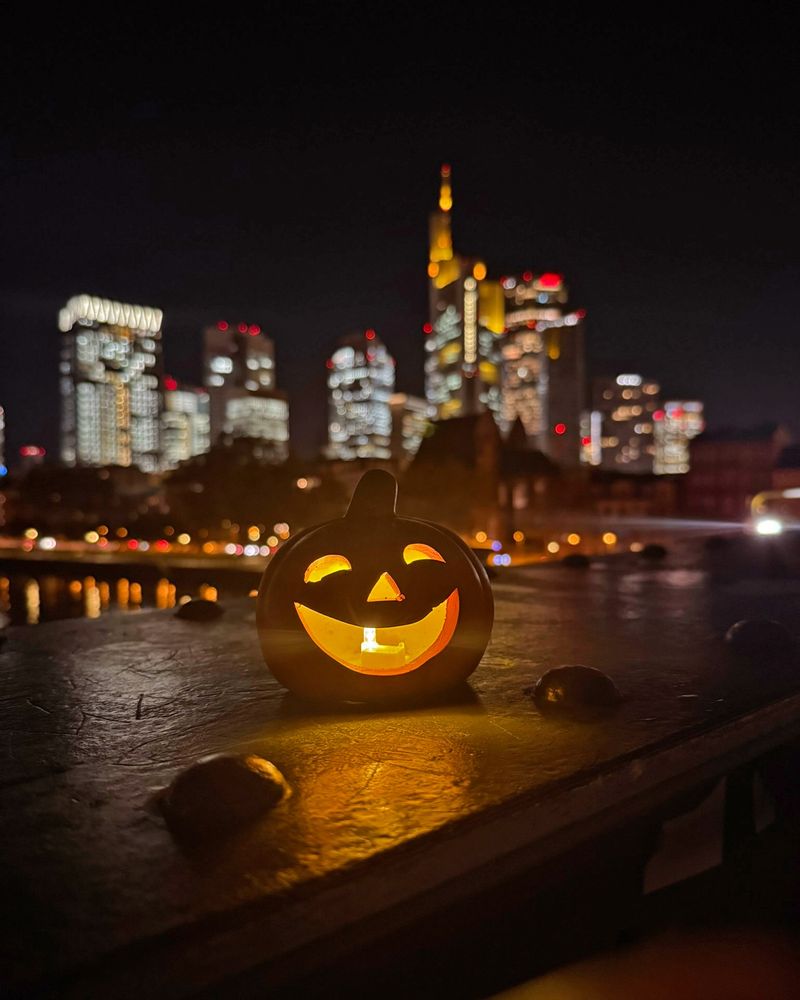 Ein Kürbis mit geschnitztem, lachendem Gesicht und leuchtendem Lämpchen vor der Frankfurter Skyline. Blick vom Eisernen Steg. 