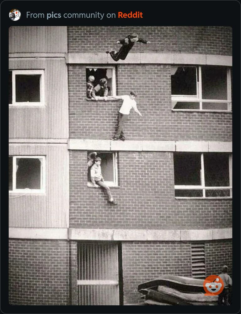 Block of flats with children jumping from windows onto stacks of mattresses. 